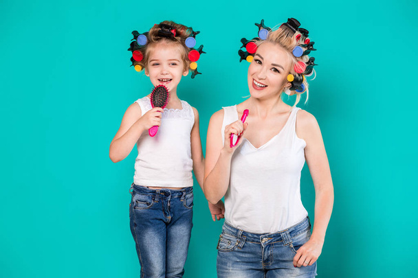 Mother and little daughter in hair curlers on a turquoise background in the studio - Foto, Imagem