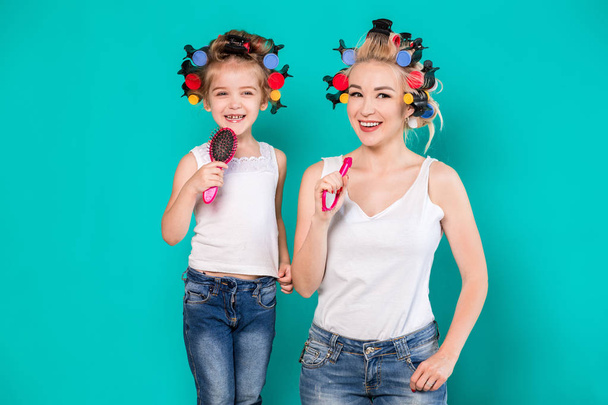 Mother and little daughter in hair curlers on a turquoise background in the studio - Photo, Image