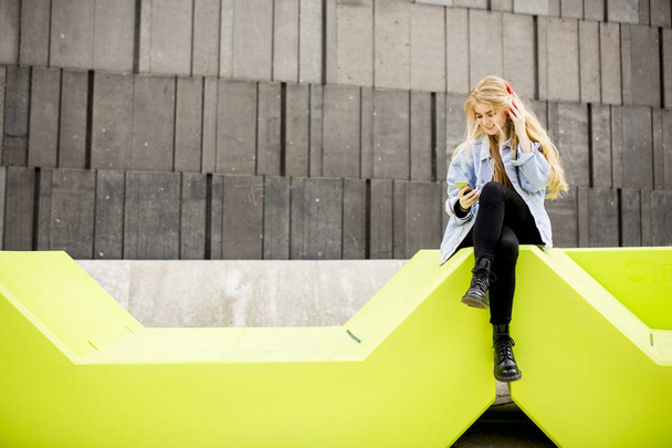 Młoda kobieta siedzi w Miasto i korzystaj z telefonu komórkowego - Zdjęcie, obraz