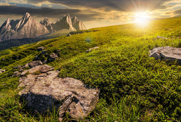 meadow with huge stones on top of mountain range at sunset - Photo, Image