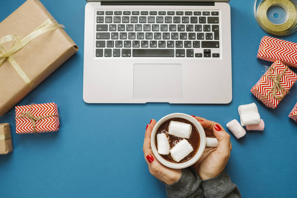 Woman hands with hot cocoa with marshmallows and laptop, gifts,  - Photo, Image