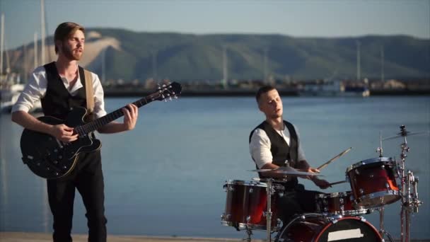 Músicos tocando bateria e guitarra durante a performance ao ar livre da banda
 - Filmagem, Vídeo