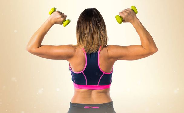 Sport woman making weightlifting on ocher background - 写真・画像