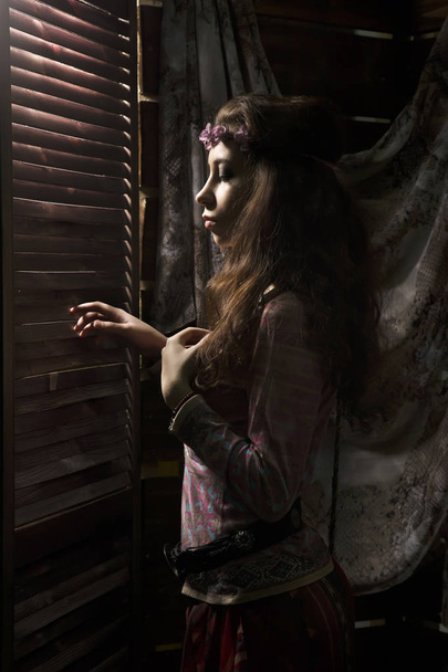 beauty hippie boho woman looks through a shuttered window on a dark background - Zdjęcie, obraz