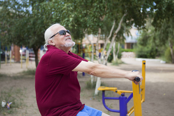 Senior man trains on sporting equipment on open air - Photo, Image