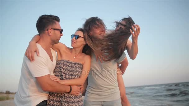 Skupina mladých lidí s divokou zubatý úsměv spolu trávili čas u moře za větrného počasí a těší na západ slunce. - Záběry, video