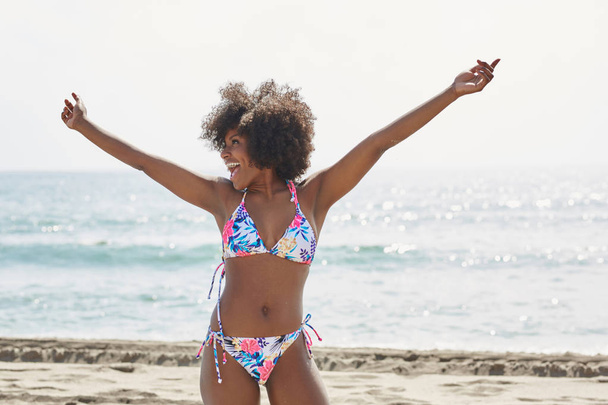 Happy afro american woman in bikini raising hands on beach - Foto, afbeelding