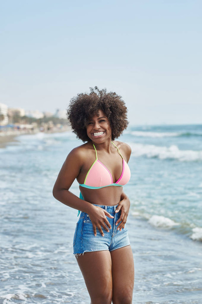 Pretty afro american girl standing in sea holding hand on stomac - Photo, image