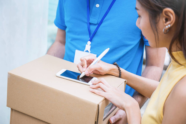 Крупным планом женщина руки добавления получил подпись после принятия доставки коробки от мужчины в синей форме
 - Фото, изображение