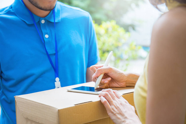 Close up woman hands appending received signature after accepting delivery of boxes from man in blue uniform - 写真・画像