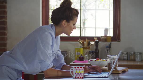 Young woman using laptop in kitchen - Filmagem, Vídeo