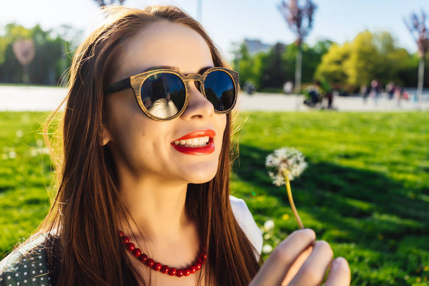 Funny smiling happy woman in sunglasses blowing dandelion - Fotó, kép