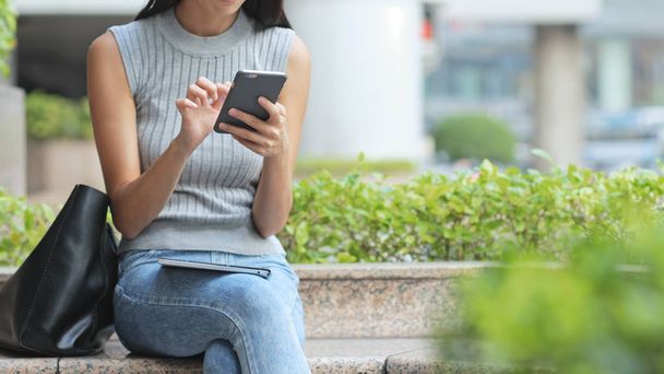 Woman using cellphone and sitting at outdoor - Photo, Image