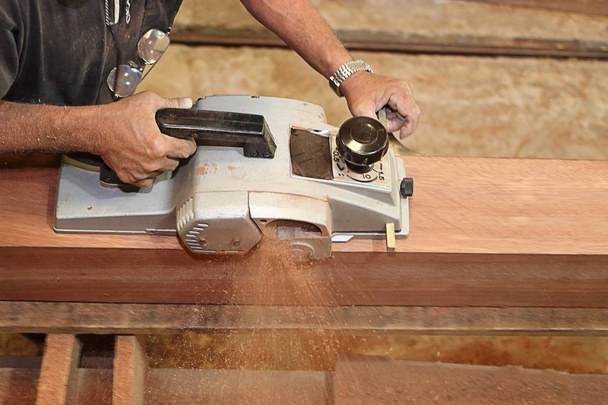 Aerial view of senior carpenter using electric planer with wooden plank in carpentry workshop. Selective focus and shallow depth of field. - Foto, imagen