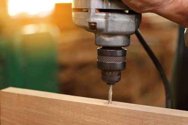 Close up broca elétrica está sendo trabalhado com placa de madeira por trabalhador. Foco seletivo e profundidade de campo rasa
. - Foto, Imagem
