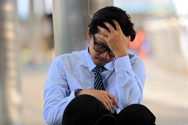 Lähikuva stressaantunut nuori aasialainen liikemies käsi otsassa istuu lattialla. Väsymys ja päänsärky työtä vastaan
. - Valokuva, kuva