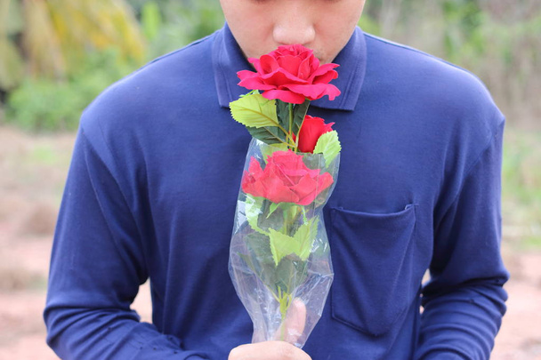 Un beau bouquet de roses rouges artificielles est tenu par un jeune homme détendu sur fond de nature floue. Concept d'amour et de romance
. - Photo, image