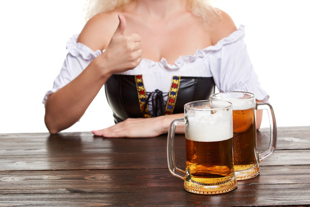 Beautiful young blond girl in traditional costume drinks out of oktoberfest beer stein. - Photo, image
