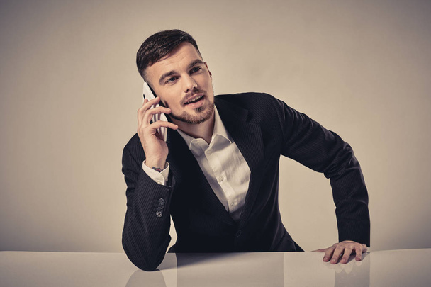 Knappe jonge man op de mobiele telefoon te praten tijdens de vergadering op zijn werkplek op kantoor - Foto, afbeelding