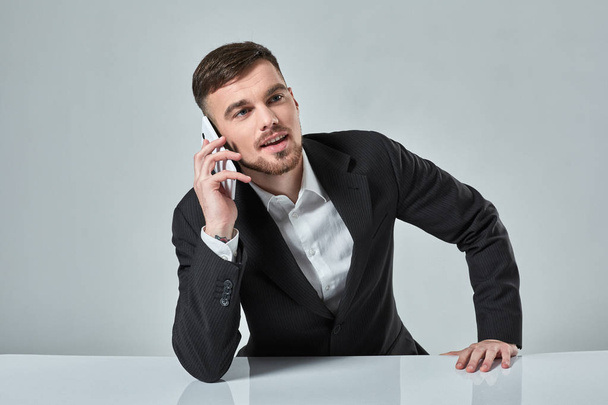 Handsome young man talking on the mobile phone while sitting at his working place in office - Fotoğraf, Görsel
