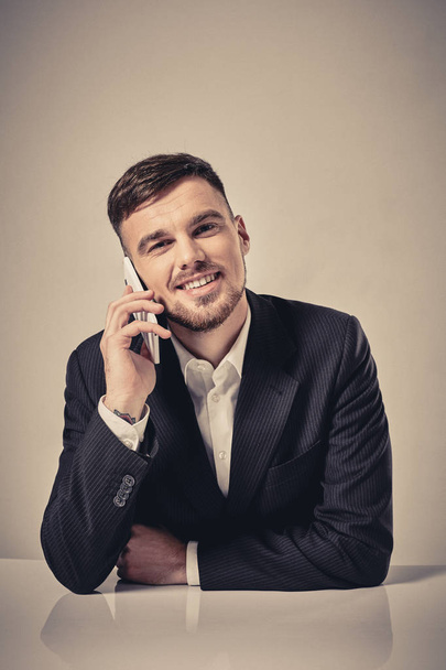 Komea nuori mies puhuu matkapuhelimella istuessaan työpaikallaan toimistossa
 - Valokuva, kuva