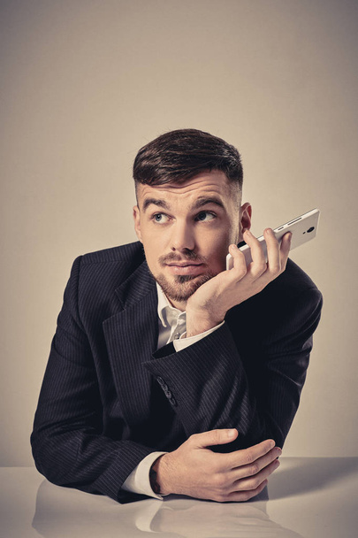 Przystojny młody mężczyzna rozmawia przez telefon komórkowy siedząc w swoim miejscu pracy w biurze - Zdjęcie, obraz