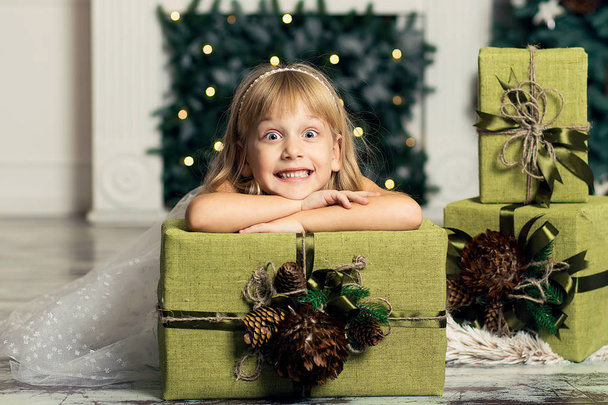 cheerful little girl is playing with gifts on the background of a Christmas tree - Fotografie, Obrázek