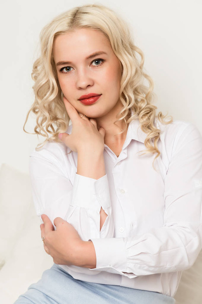 Beautiful young blonde woman in a white blouse sitting on a sofa - Foto, Imagem
