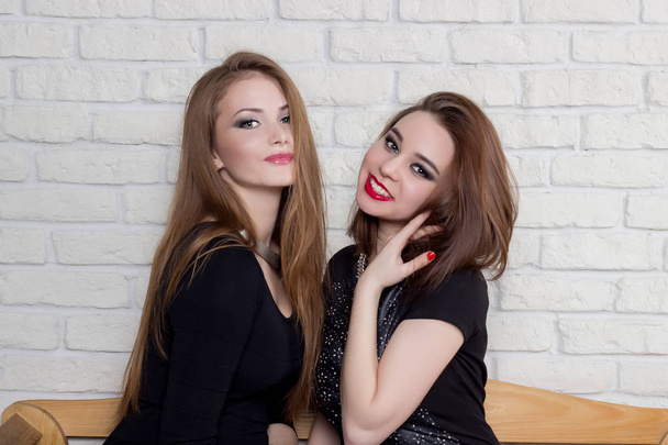 two beautiful young girls in black dresses sit on the bench and gossip - Foto, Imagem