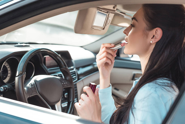 Mujer aplicando lápiz labial en el coche
 - Foto, imagen