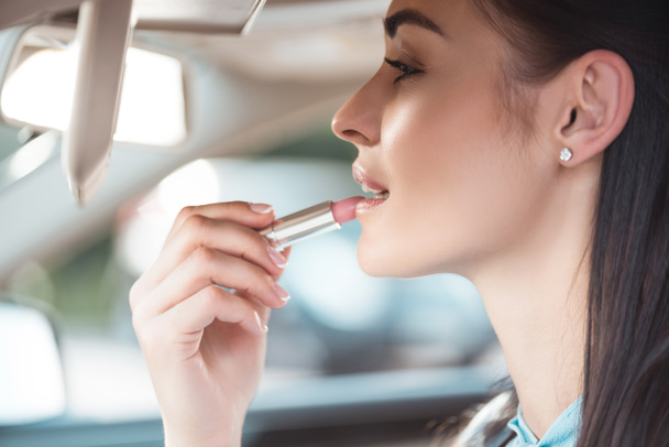 Vrouw toepassing lippenstift in auto - Foto, afbeelding