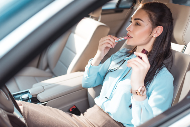 Mujer aplicando lápiz labial en el coche
 - Foto, imagen