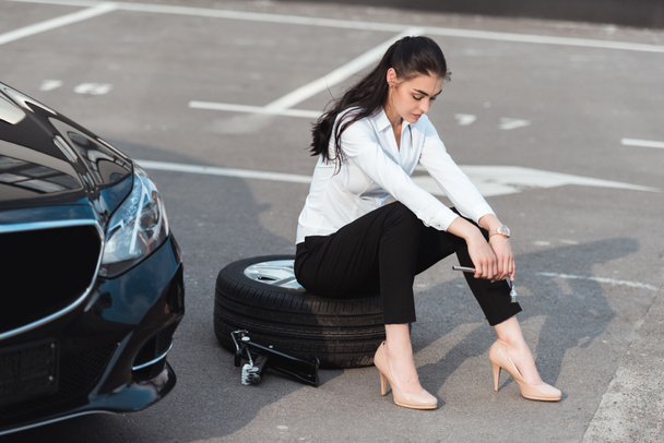 mujer sentada sobre un neumático con llave inglesa
 - Foto, Imagen