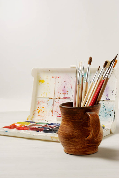 Pinturas de acuarela brillantes y pinceles usados para pintar sobre una superficie de mesa de madera. Vintage tonificado foto
 - Foto, imagen