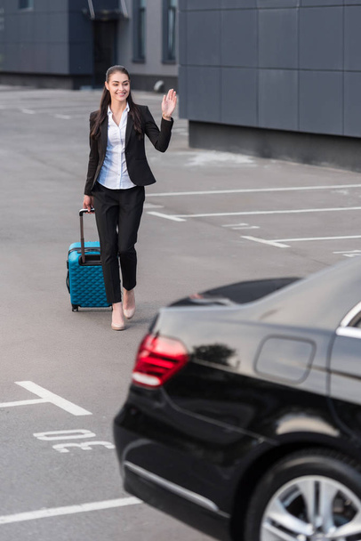 Woman walking with suitcase in parking lot - Foto, imagen