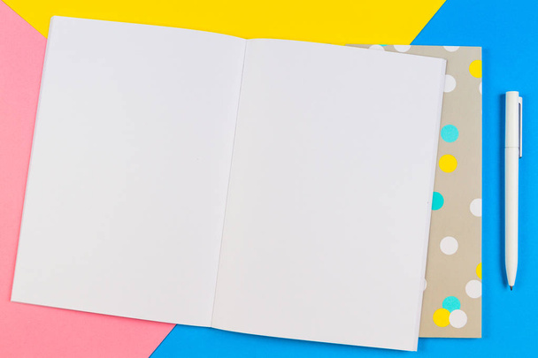 Cuaderno de papel en blanco abierto con lápiz sobre fondo azul, amarillo y rosa
. - Foto, Imagen
