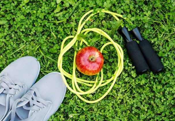 Кросівки, яблуко і мотузка на свіжій зеленій траві
 - Фото, зображення