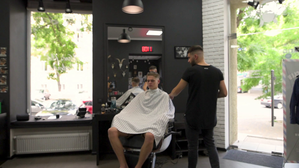 Barber az ügyfél combs hajvágás során, és fordul a karosszékben, amely különböző oldalról a fodrász - Felvétel, videó