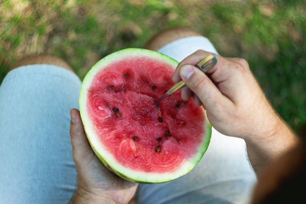 A young man is eating a watermelon with a spoon. The concept of  - Фото, зображення