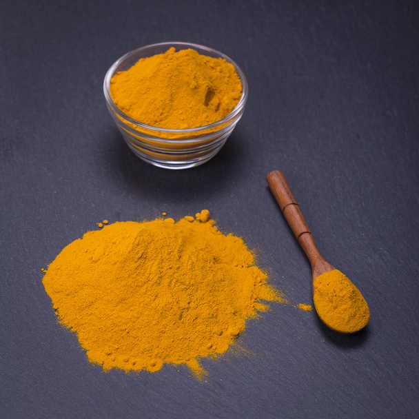 Organic turmeric, curcuma powder on black slate platter background. Curry powder - 写真・画像