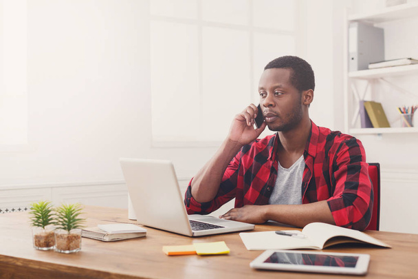 junger schwarzer Geschäftsmann telefoniert mit Handy in modernem weißen Büro - Foto, Bild