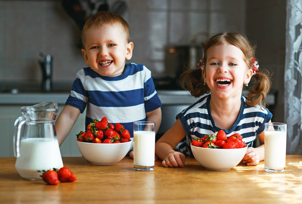 Happy children brother and sister eating strawberries with milk - Fotó, kép