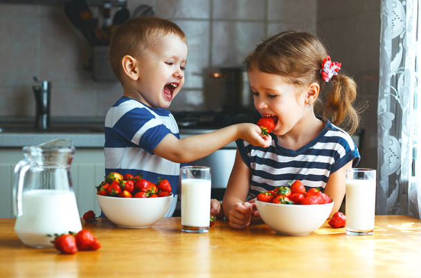 Happy children brother and sister eating strawberries with milk - Zdjęcie, obraz