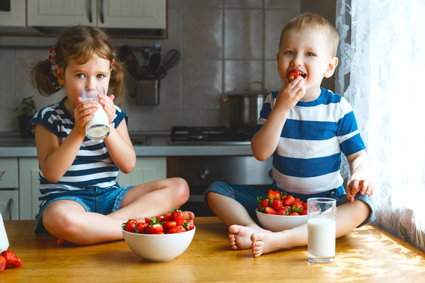 Onnelliset lapset veli ja sisko syövät mansikoita maidon kanssa
 - Valokuva, kuva