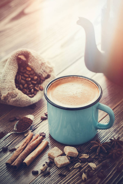 Espresso-Kaffee in blau emaillierter Tasse, Zuckerwürfel, Sack Kaffeebohnen und Gewürze auf Holzbrett. Retro stilisiert. - Foto, Bild