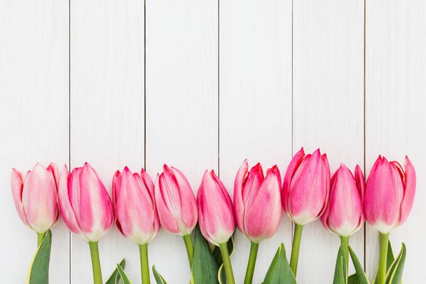 Rand van roze tulpen op witte houten achtergrond. Bovenaanzicht - Foto, afbeelding