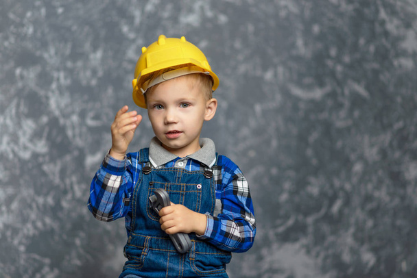the boy in yellow hard hat holding a pipe wrench in the hands - Foto, afbeelding