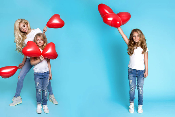 Beautiful blonde mother and daughter stand on a blue background and holding red Valentine's balloons - Photo, Image