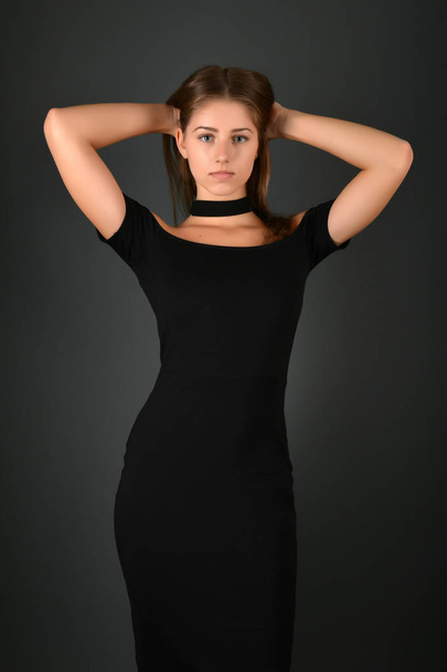 Fiatal barna hölgy fekete ruhában pózol a szürke háttér - Fotó, kép