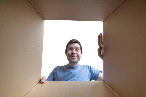Gelukkig jongeman is opening geschenk en op zoek in kartonnen doos - Foto, afbeelding